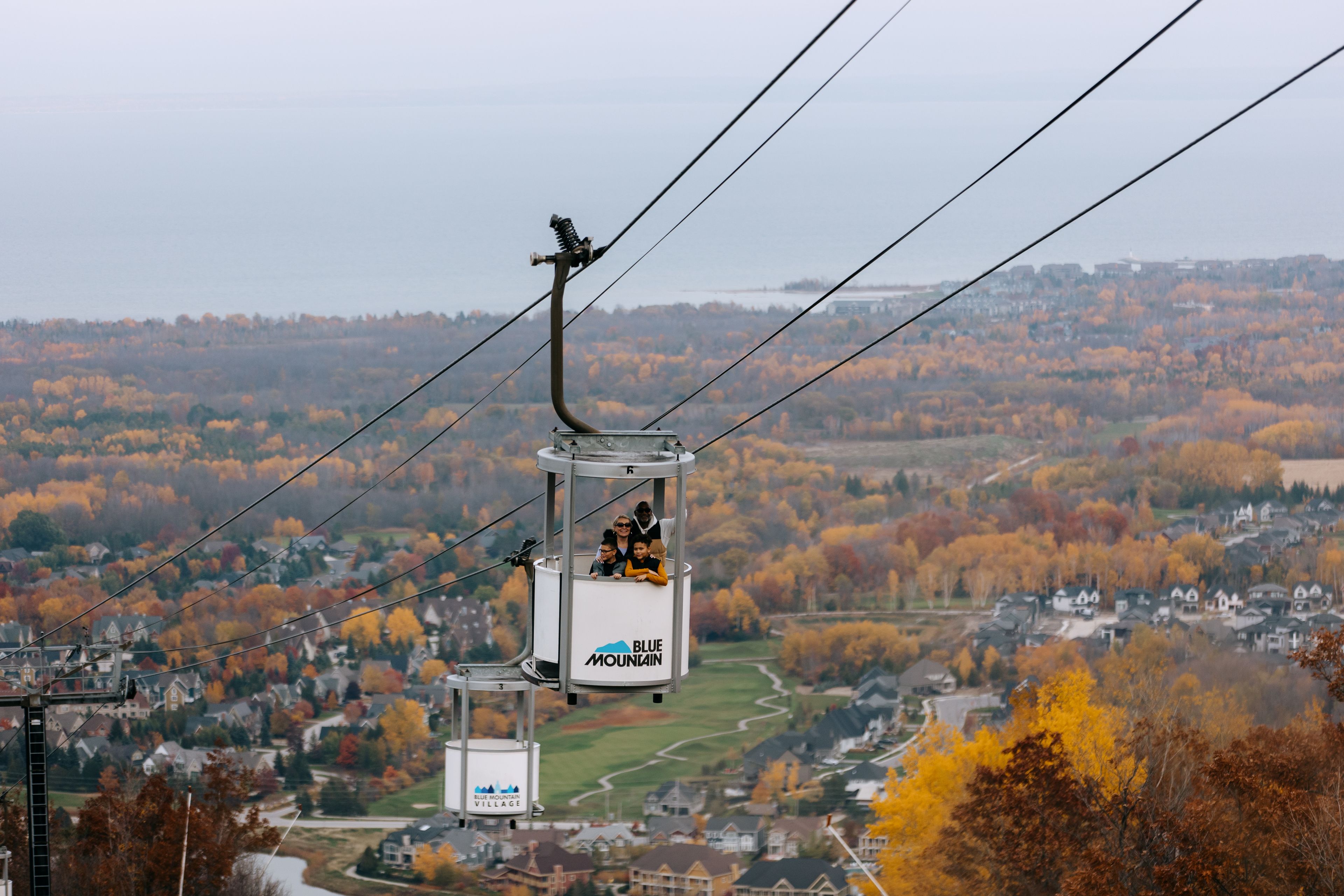 A family of four ascends up Blue Mountain Resort on the Open-Air Gondola, taking in the stunning views of the fall foliage and forests below. 